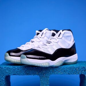 Air Jordan 11 High preto e branco, com couro envernizado brilhante, solado translúcido e o icônico logotipo Jumpman na lateral, visto de perfil