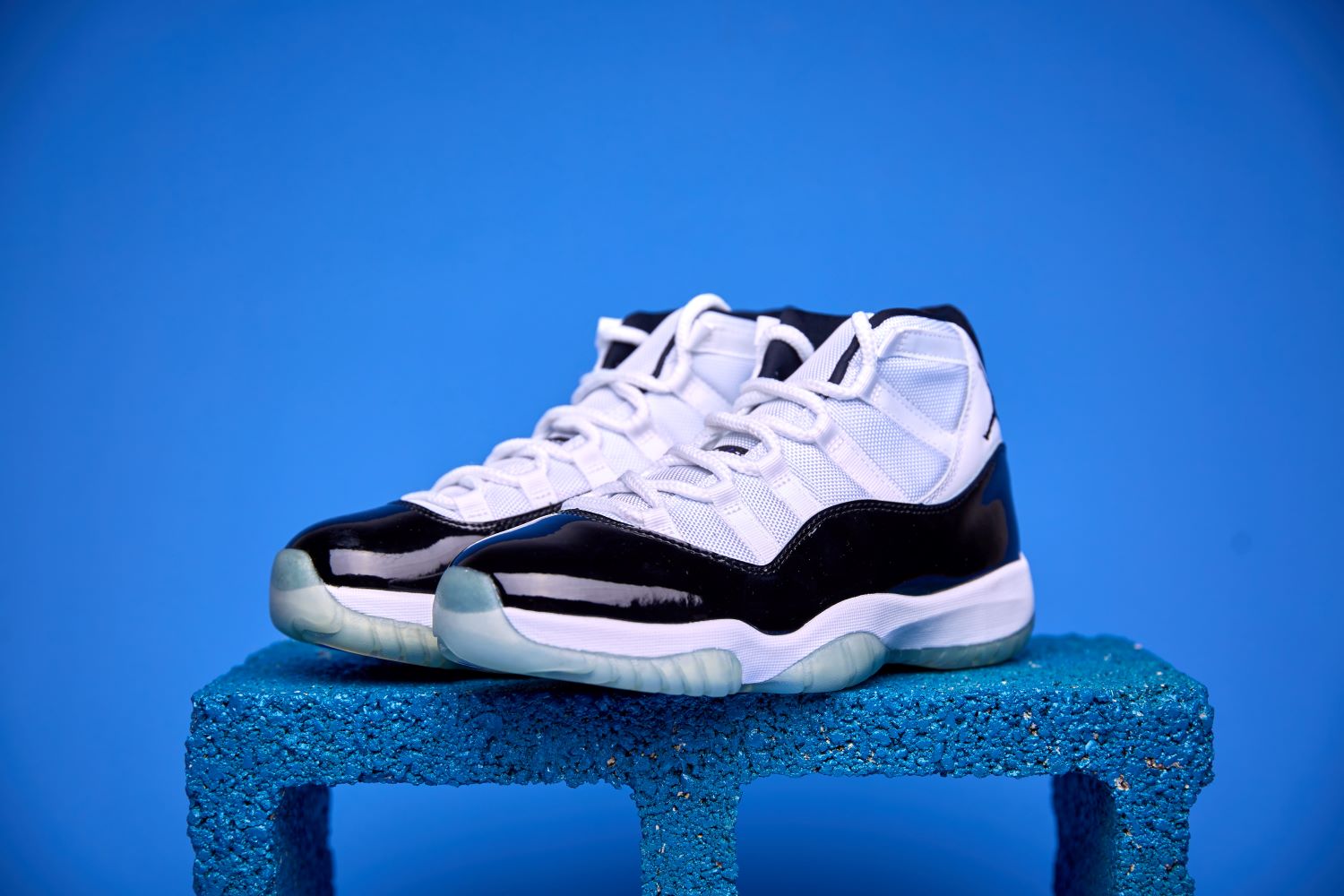 Air Jordan 11 High preto e branco, com couro envernizado brilhante, solado translúcido e o icônico logotipo Jumpman na lateral, visto de perfil