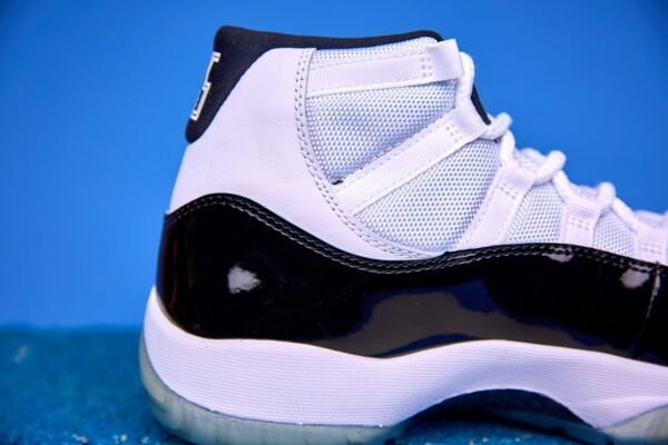 Air Jordan 11 High preto e branco, com couro envernizado brilhante, solado translúcido e o icônico logotipo Jumpman na lateral, visto de perfil
